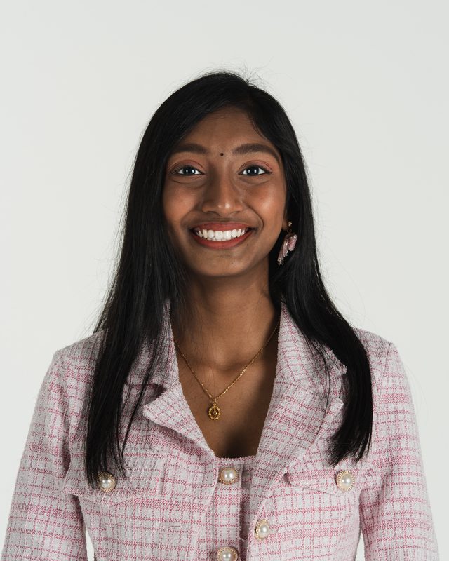 Roma smiling in a pink tweed jacket