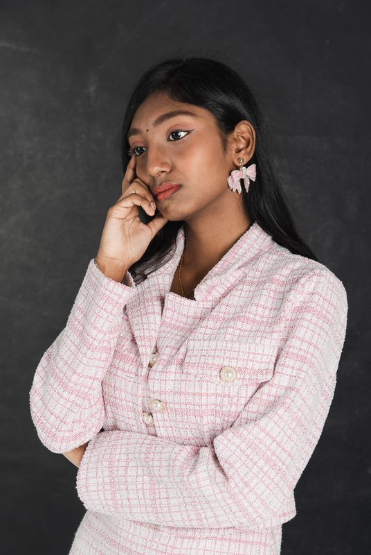 Roma with a hand at her cheek on a dark backdrop