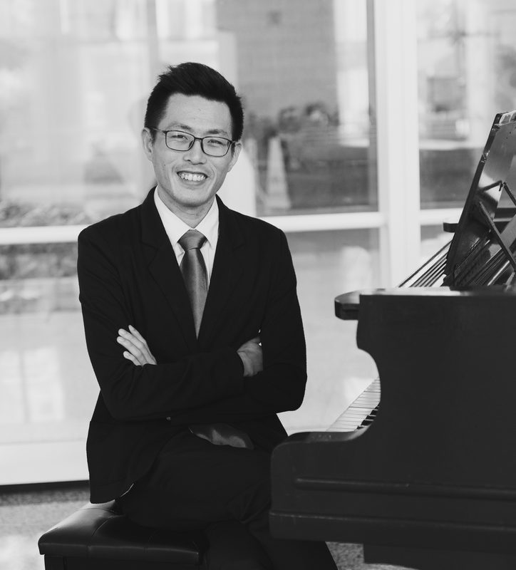Tony seated by a grand piano with arms crossed, black and white