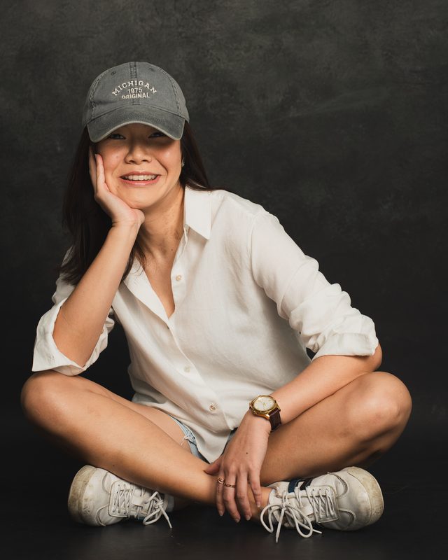 Wylie in a cap, sitting cross-legged on a dark backdrop